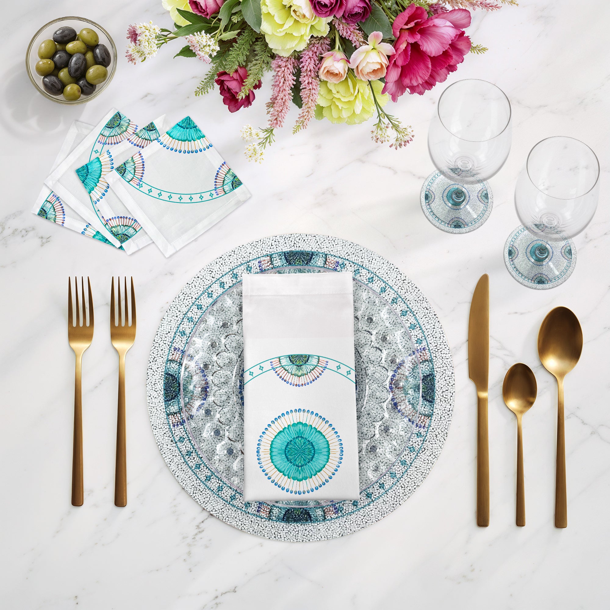 Dining table setting with decorative plates, cutlery, and flowers on a marble surface.