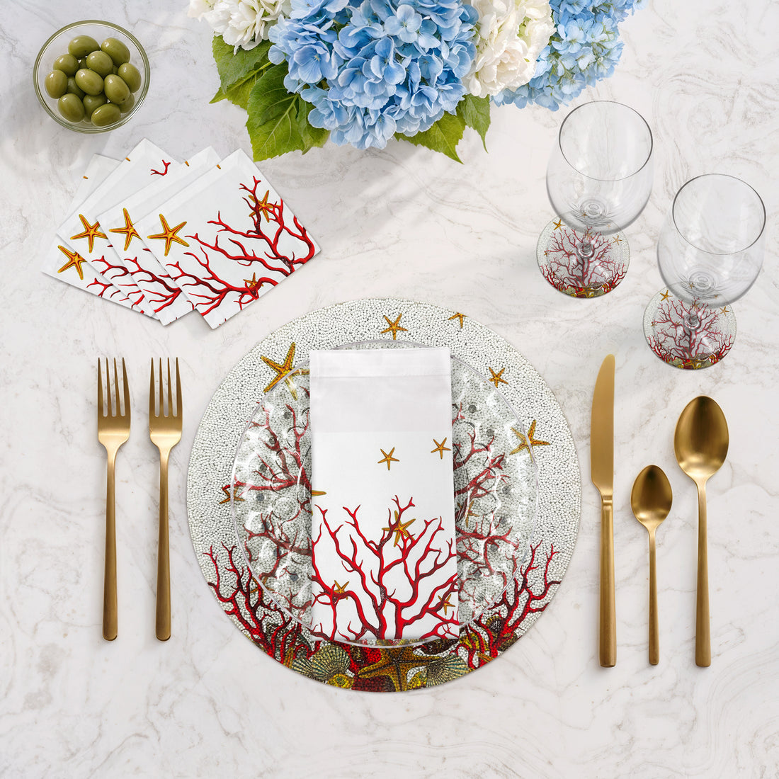 Table setting with coral-themed plates, napkins, and cutlery on a marble surface.
