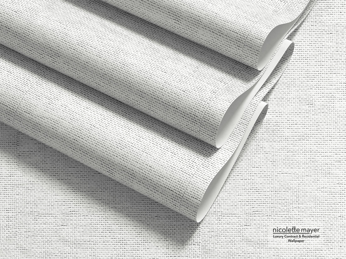 Three rolled sheets of textured wallpaper with a fine gray and white linen-like pattern, arranged diagonally on a matching flat surface. The brand name &