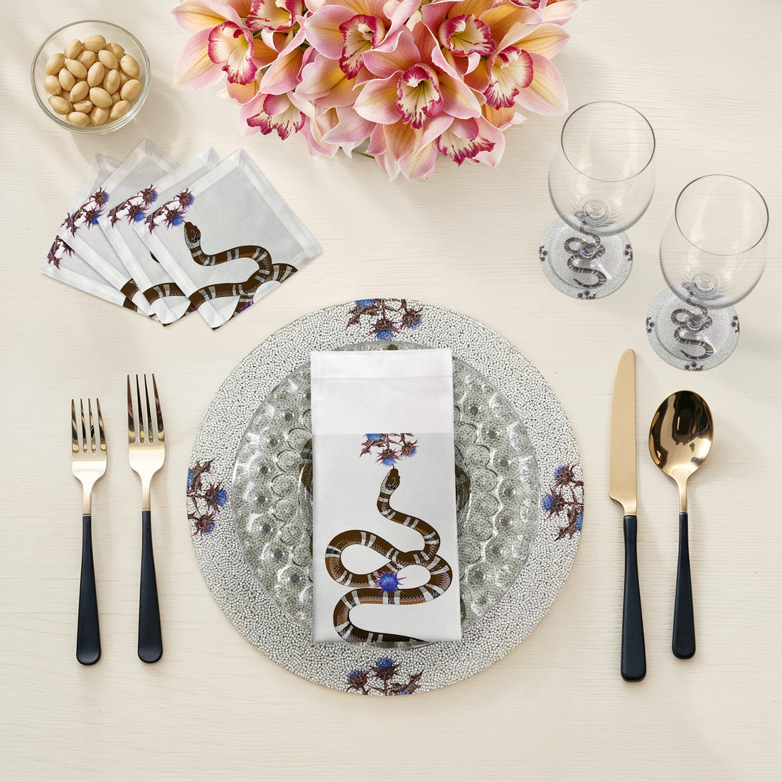 Table setting with snake-themed napkins, cutlery, and glasses on a neutral background
