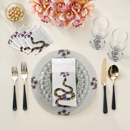 Table setting with snake-themed napkins, cutlery, and glasses on a neutral background