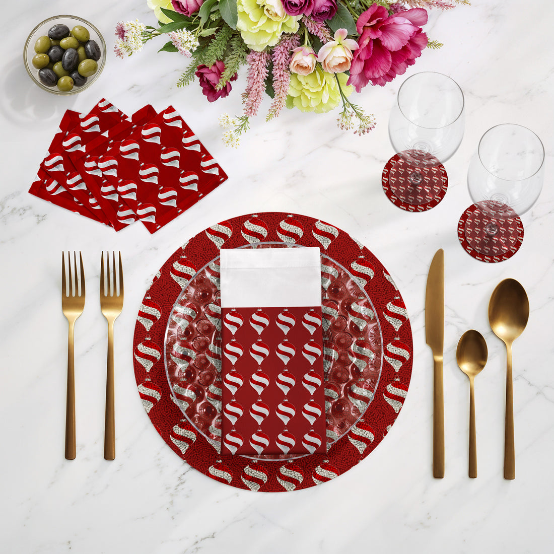 Dining table setting with red and white patterned plates, gold cutlery, and flowers on a marble surface.